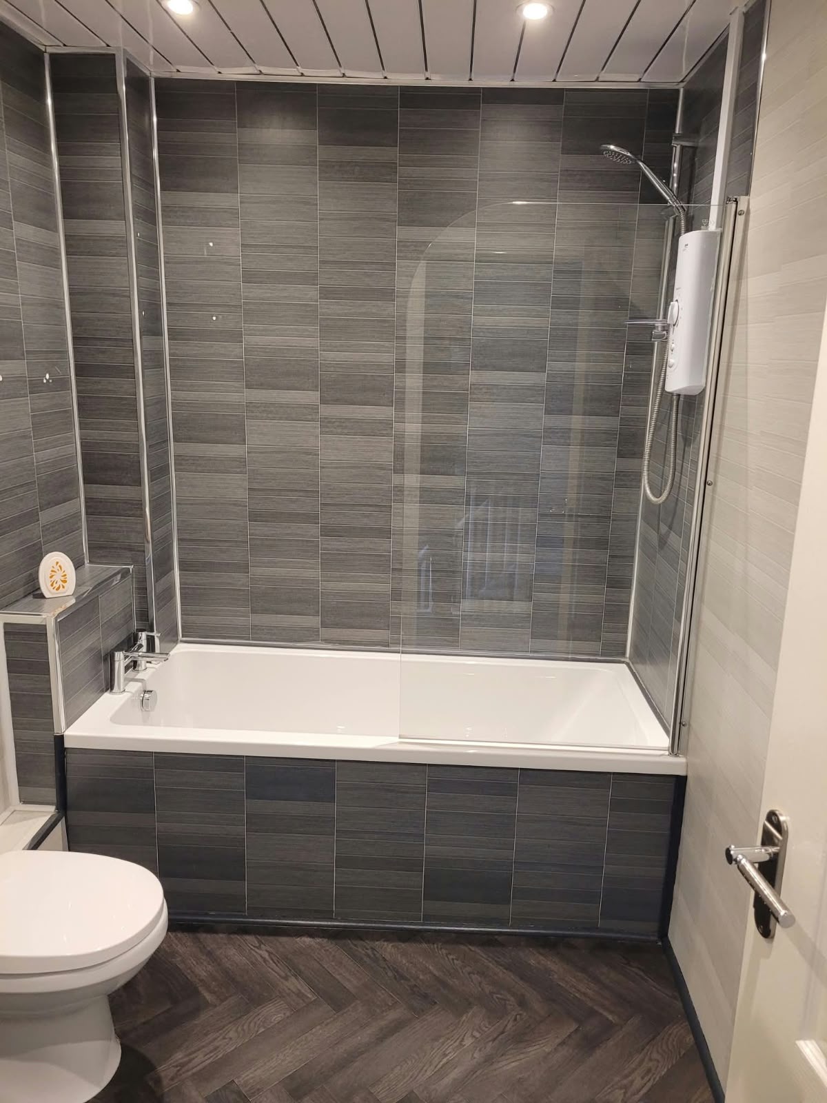 Bathroom with slate tiled walls, a bath with curved screen and herringbone flooring